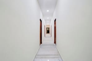 A long, narrow hallway with white walls and a marble floor, leading to a door at the end.