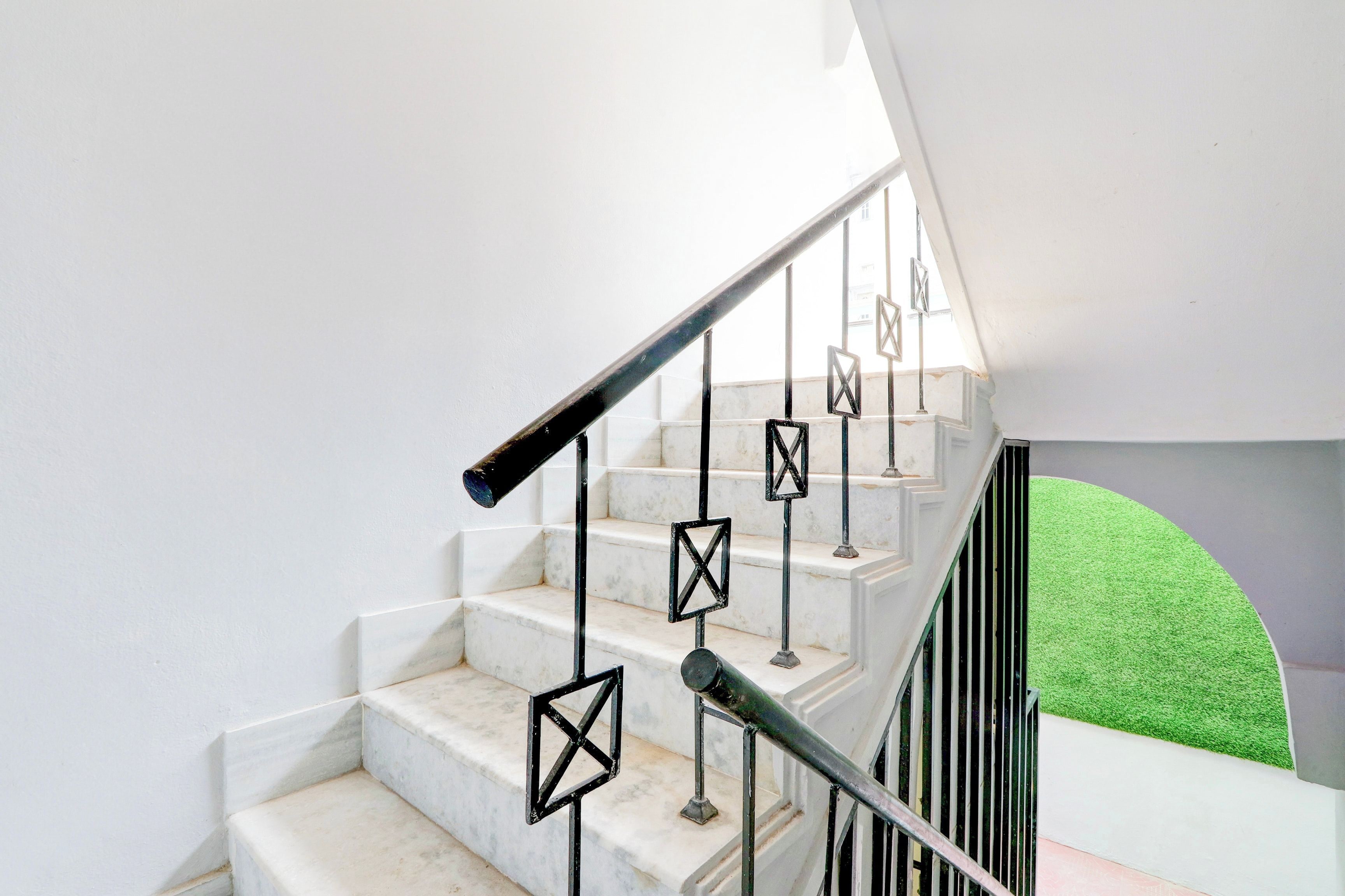 Una escalera con escalones de mármol blanco y barandillas de metal negro.