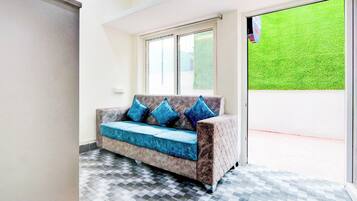 Una habitación con sofá, piso a cuadros, ventana y vista a un césped verde.