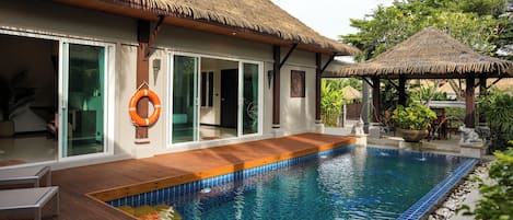 A poolside area with a wooden deck, a thatched-roof structure, and a lifebuoy.