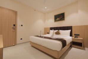 Una camera d'albergo con un letto grande, un armadio in legno, un quadro appeso al muro e un comodino con telefono e caricabatterie.
