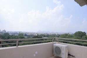 Terrat amb una unitat de climatització, una barana i una vista de paisatge urbà amb edificis i arbres.