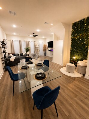 A modern living room with a glass dining table, blue chairs, a grey sofa, and a Christmas tree. - Charming 3-bedroom townhome 11 min from Downtown Houston (Houston)