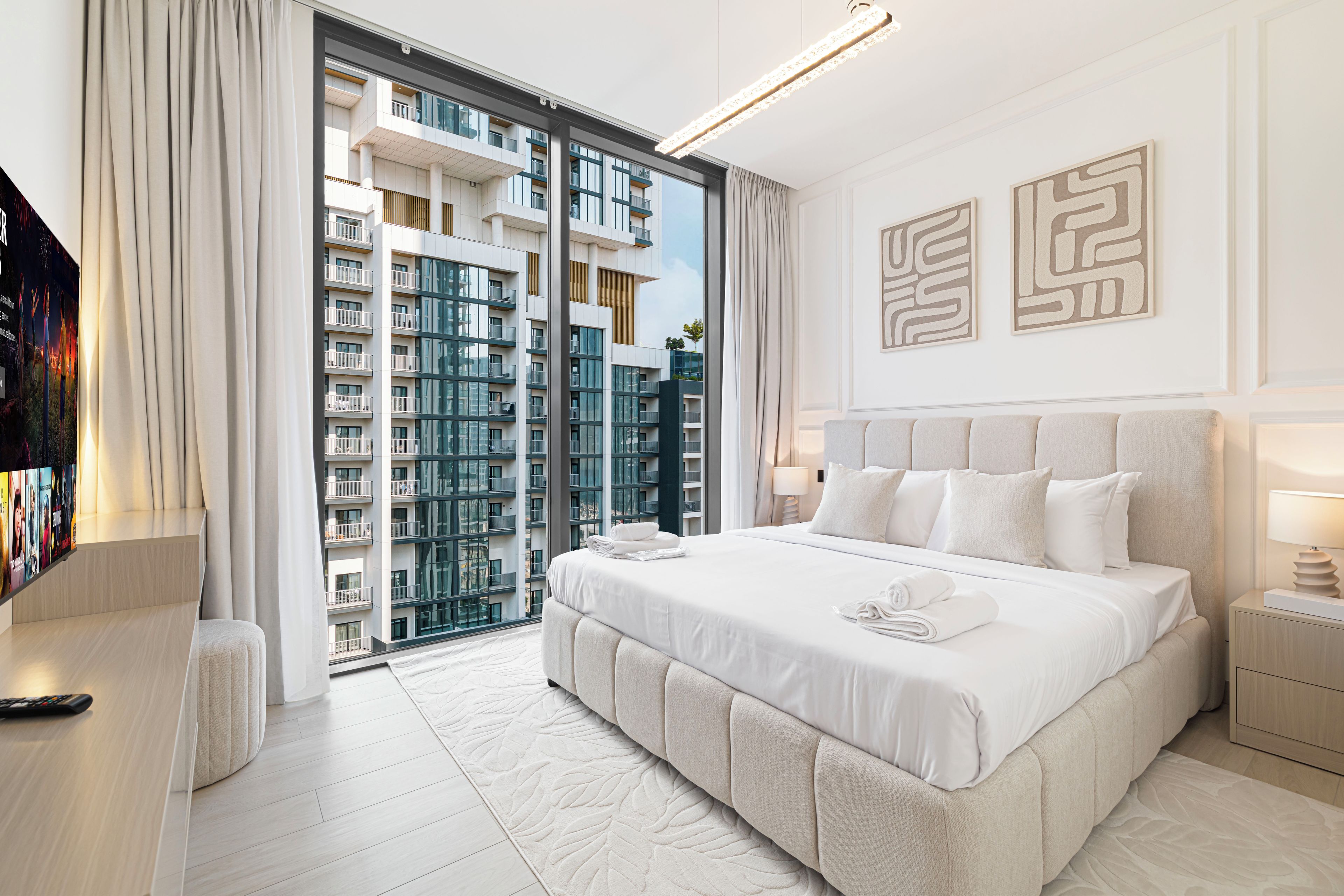A modern hotel room with a large bed, a TV, and a view of the cityscape.