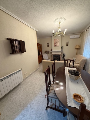 A dining area with a wooden table, chairs, a chandelier, a fireplace, and a radiator.