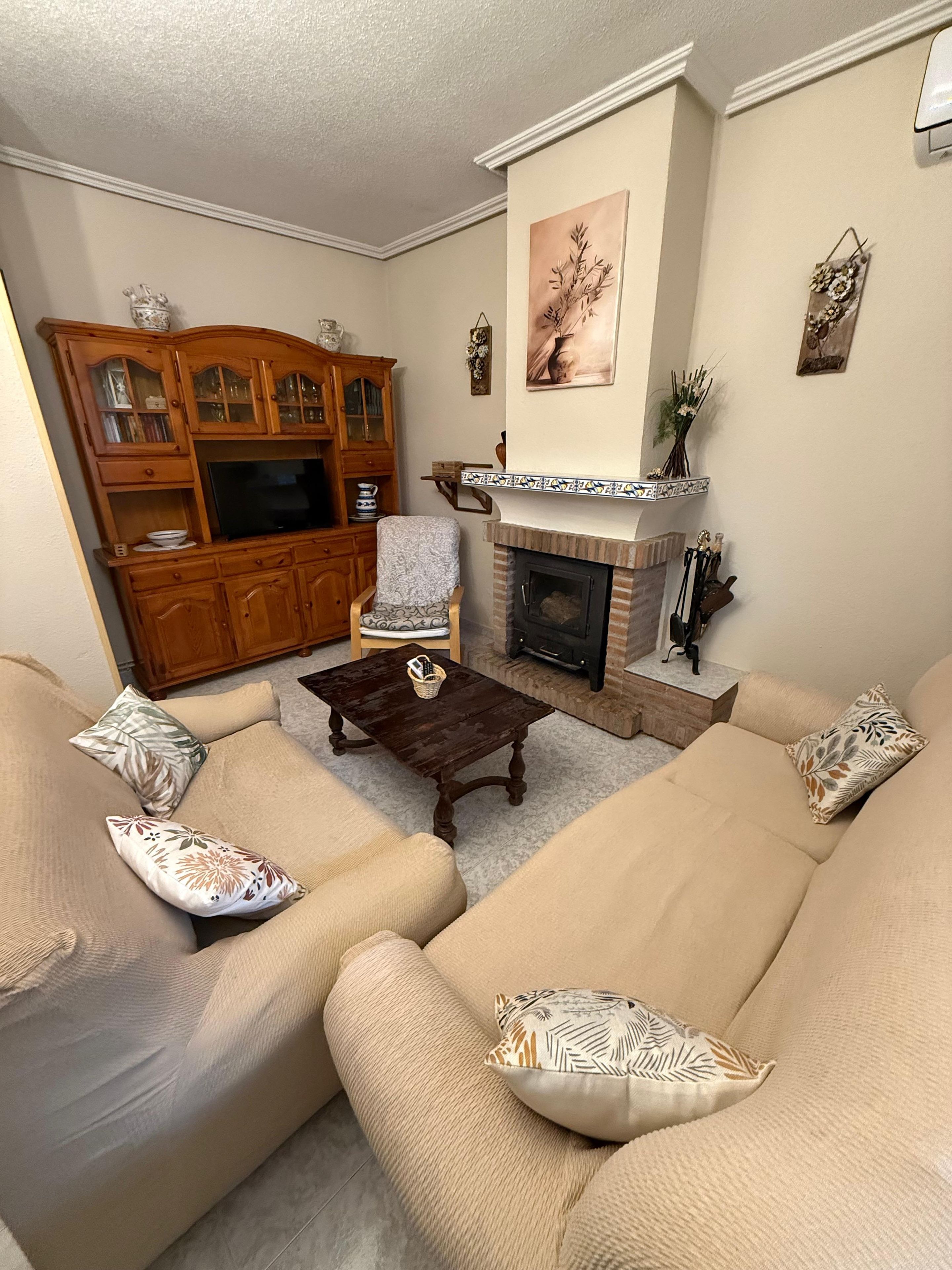 A living room with a beige sofa set, a wooden entertainment center, a fireplace, and a patterned throw pillow.