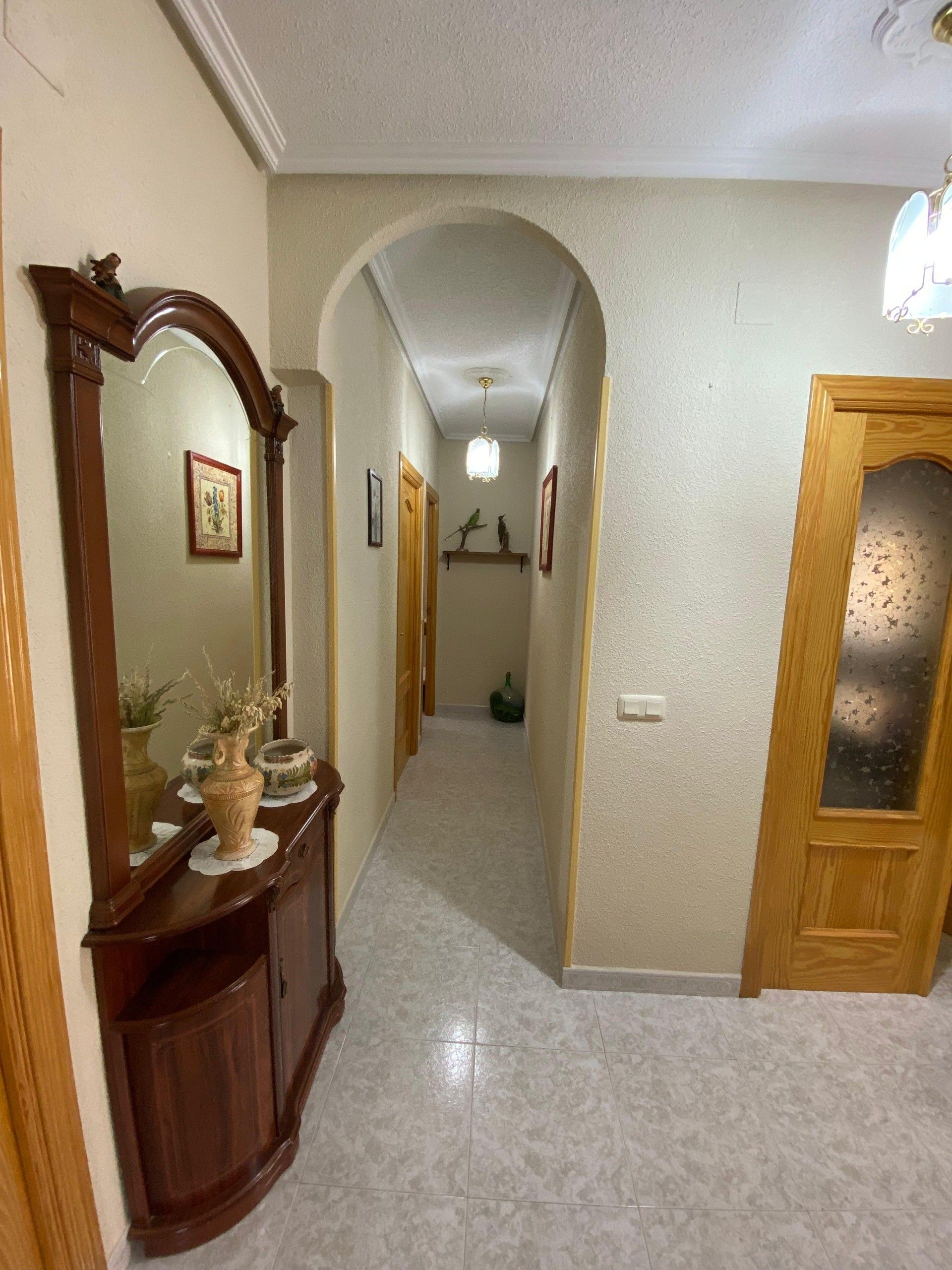 A hallway with a wooden door, a mirror, and a vase on a console table.