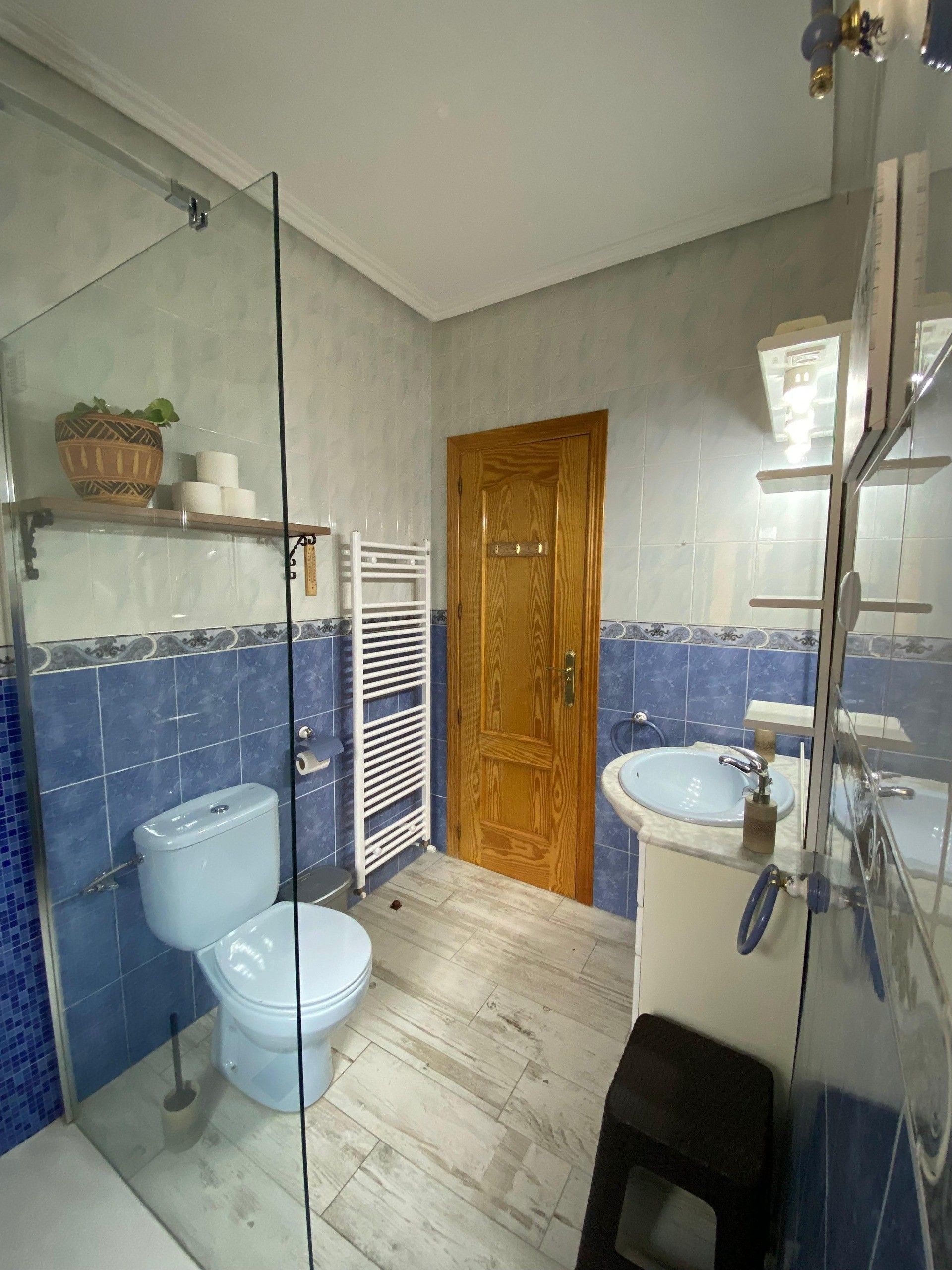 Un baño con inodoro, bidé y lavamanos, una puerta de madera y una cabina de ducha de vidrio.
