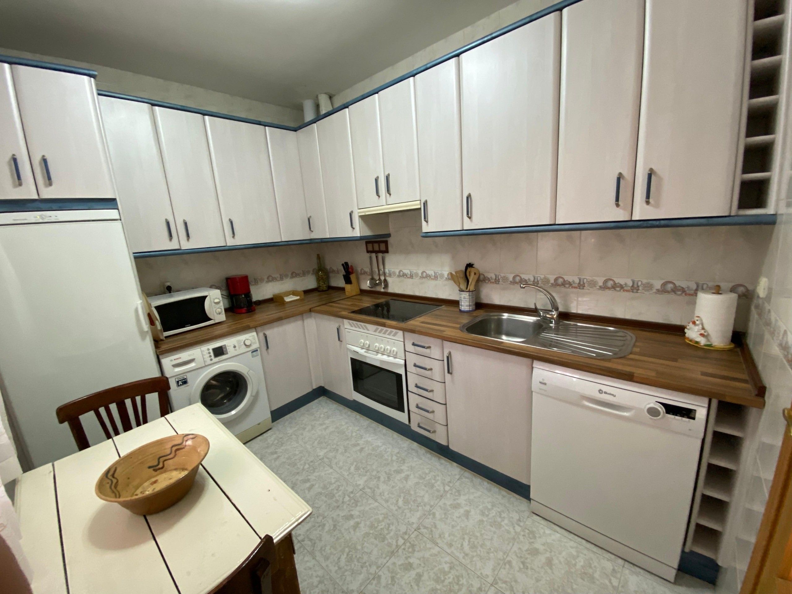 A compact kitchen with white cabinets, a microwave, a coffee maker, a sink, and a dishwasher.