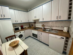 Una cocina compacta con armarios blancos, microondas, cafetera, pileta y lavavajillas.