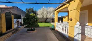 Un patio con un sendero empedrado, un árbol pequeño y un edificio amarillo con un balcón blanco.