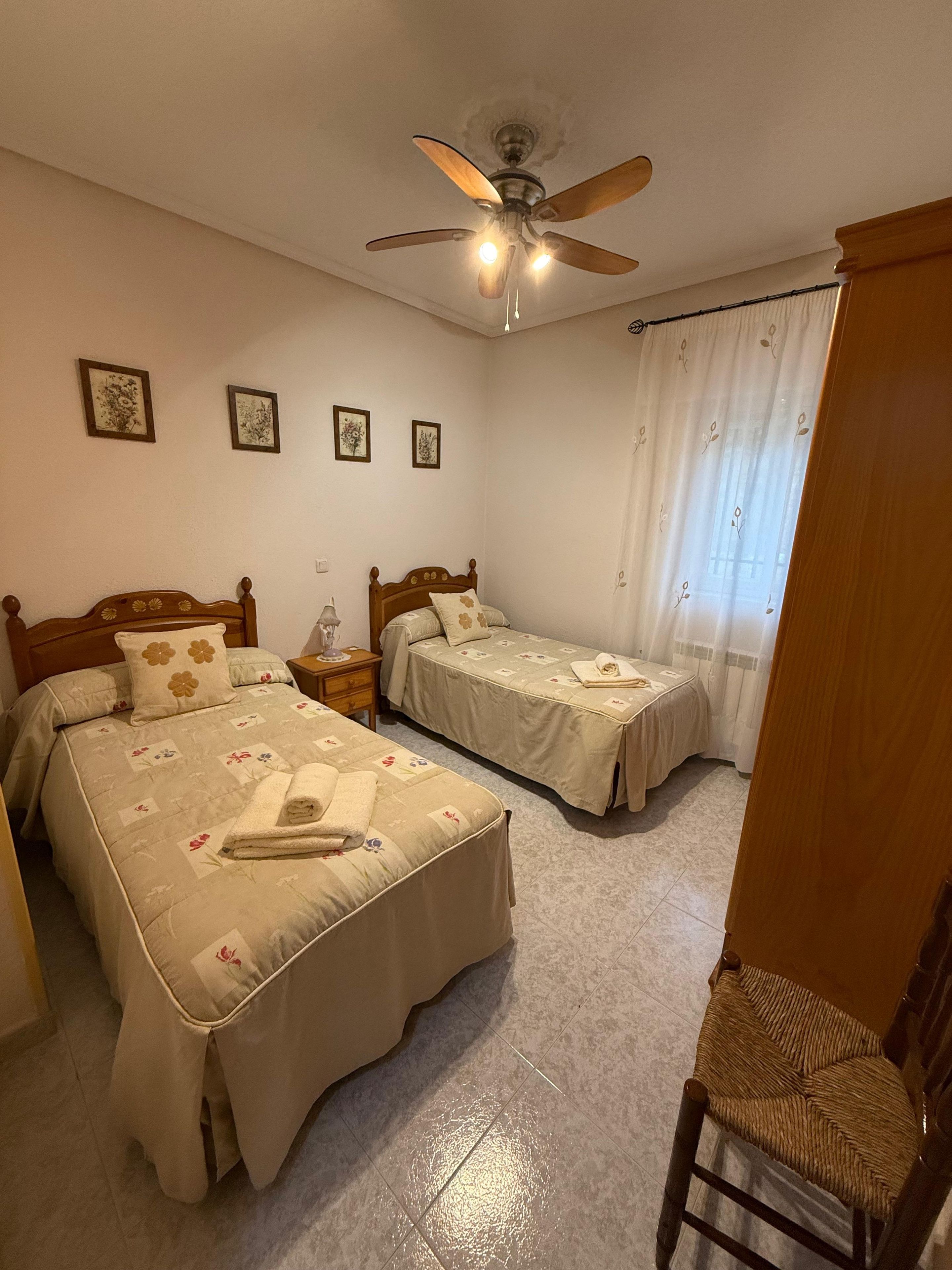 Un dormitorio con dos camas, ventilador de techo y ventana con cortinas.