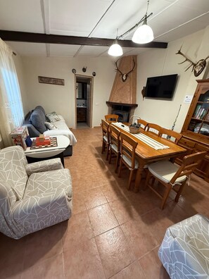 A living room with a fireplace, a television mounted on the wall, and a dining area with wooden furniture. - Country House 'La Casita Del Gévalo' with Mountain View, Wi-Fi and Air Conditioning (Piedraescrita)