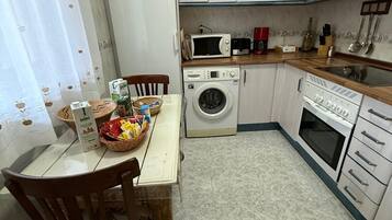 Una cocina con lavadora, microondas y estufa. Hay una mesa con sillas y una cesta con objetos.
