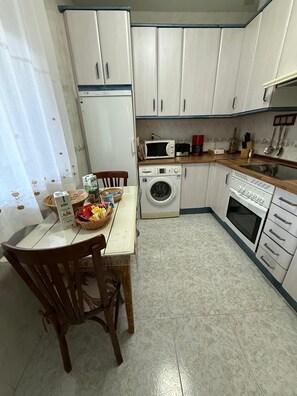 A kitchen with a washing machine, microwave, and stove. There is a table with chairs and a basket of items. - Country House 'La Casita Del Gévalo' with Mountain View, Wi-Fi and Air Conditioning (Piedraescrita)
