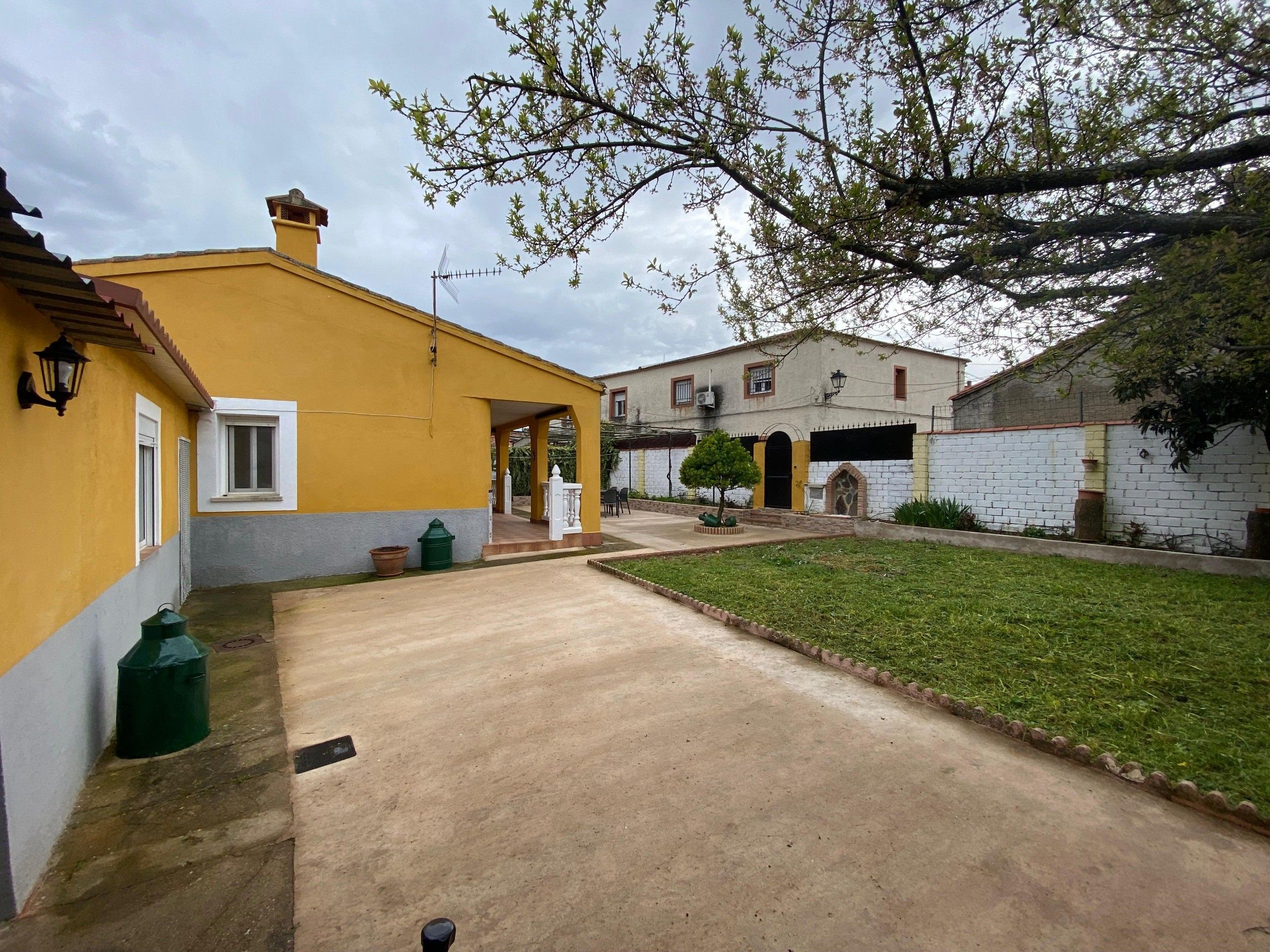 Una zona residencial con un edificio amarillo, un camino de entrada pavimentado y un pequeño jardín.