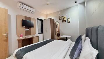 A hotel room with a bed, a desk, a wardrobe, a television, and wall-mounted artwork.