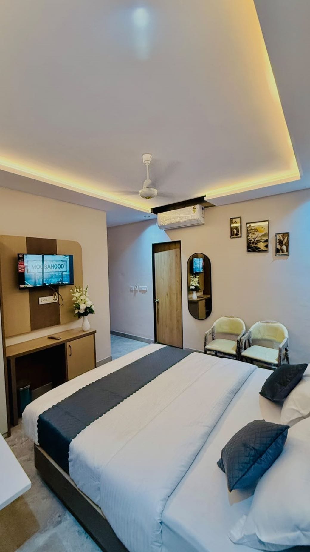 A hotel room with a bed, a desk, a television, a ceiling fan, and a door.