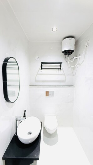 Un bagno moderno con lavandino bianco, WC, specchio e porta carta igienica a soffitto.