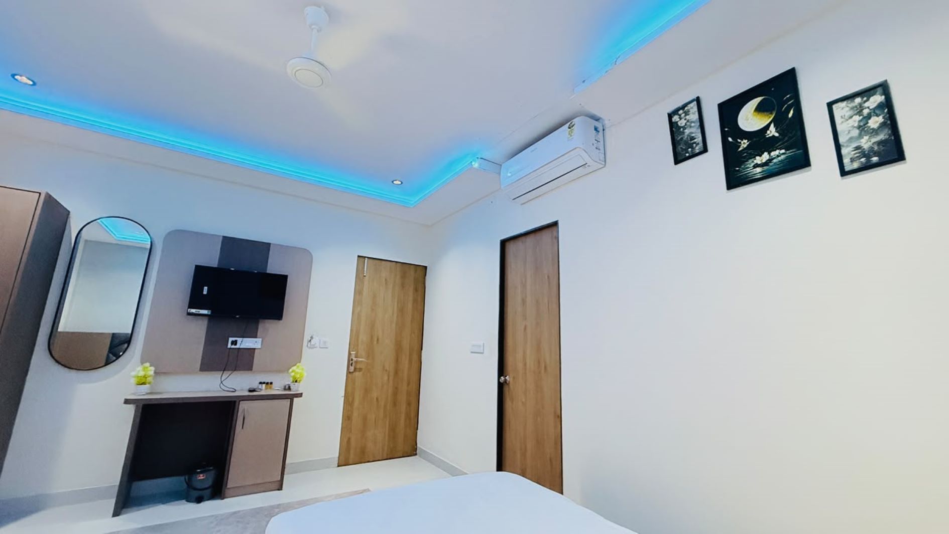 A modern bedroom with a bed, a TV mounted on the wall, a wardrobe, and a desk with a mirror.
