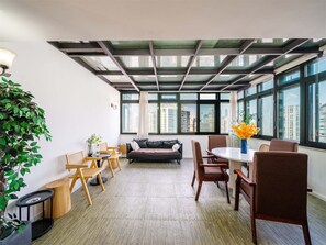 Ein modernes Interieur mit hoher Decke, großen Fenstern, einem runden Tisch und Sitzmöbeln.