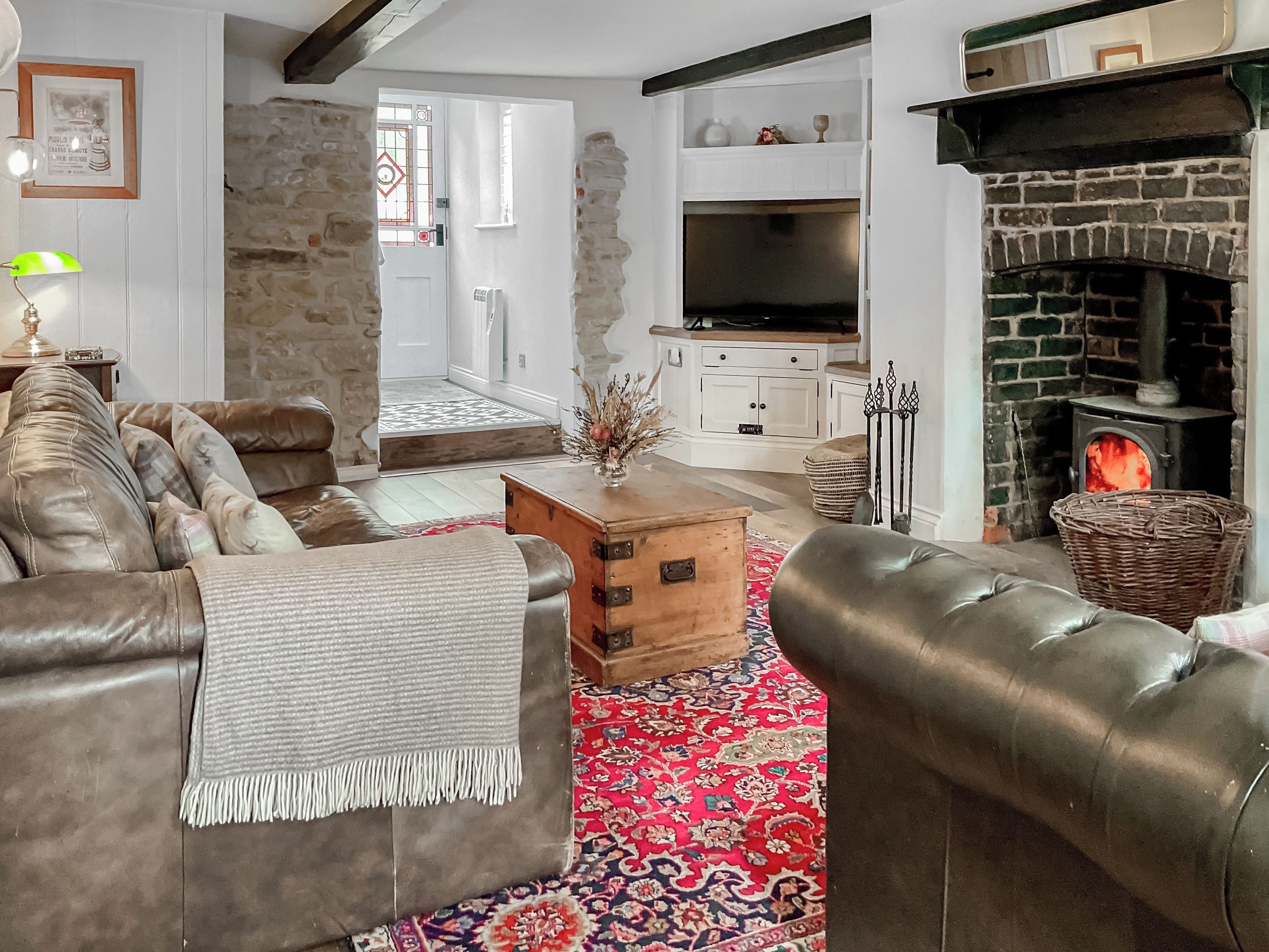 Un salon chaleureux avec des canapés en cuir, une table basse en bois, un tapis rouge à motifs, un mur en pierre, une cheminée et un téléviseur.