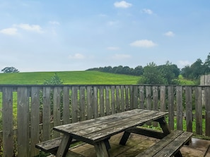Ein Holztisch mit Bänken, vor einer Holzlattenzaun und einem grünen Feld.