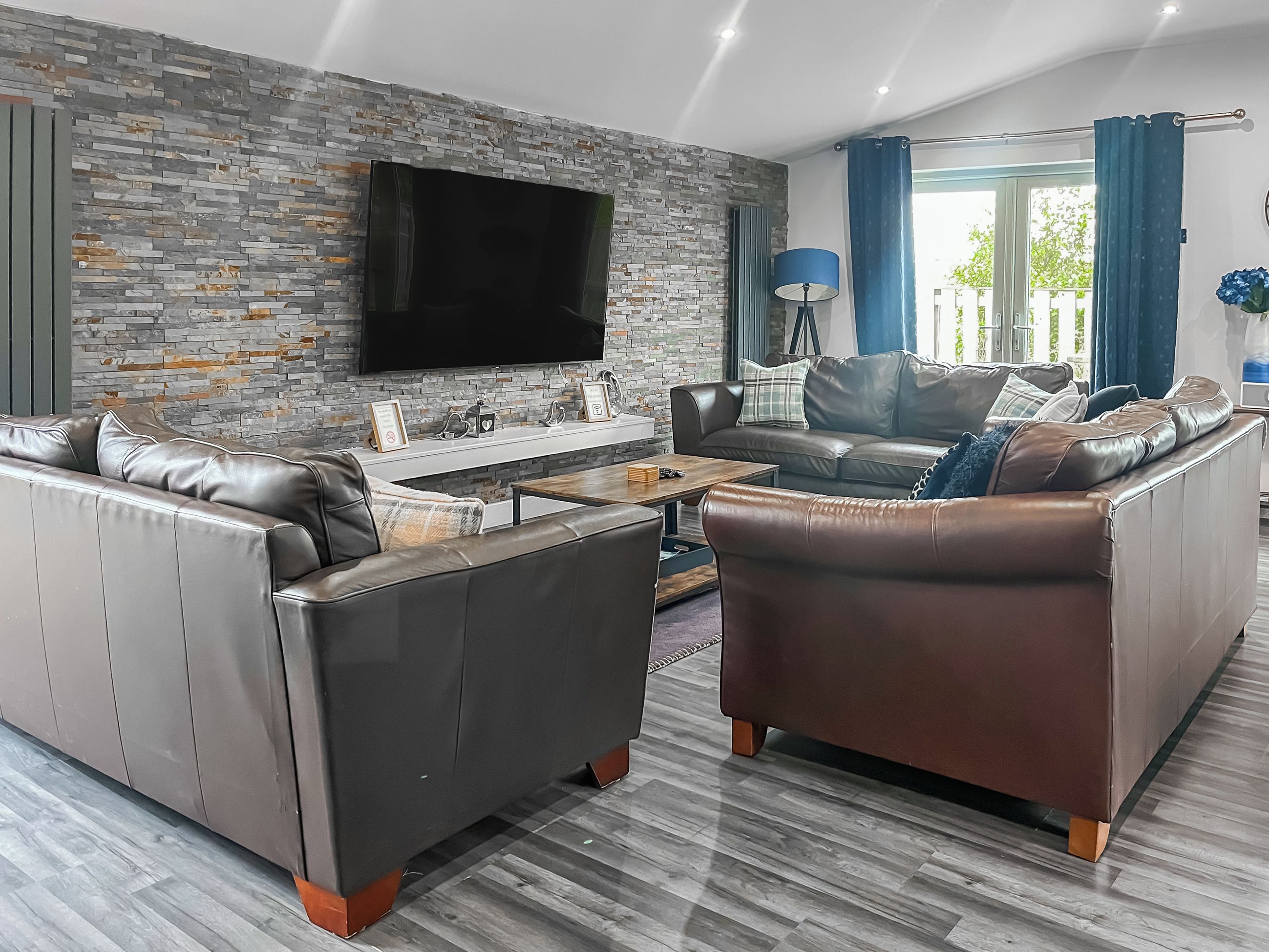 A modern living room with leather sofas, a flat-screen TV, and a stone wall.