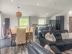 A modern living room with a black leather sofa, a dining area with wicker chairs, and a kitchen with built-in appliances. - The Wenning - UK52367 (Kirkby Lonsdale)