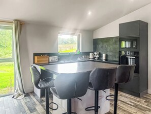 A modern kitchen with a central island, bar stools, a built-in microwave, and a view of greenery outside. - The Wenning - UK52367 (Kirkby Lonsdale)