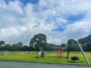 A playground with swings and a slide, surrounded by grass and trees. - The Wenning - UK52367 (Kirkby Lonsdale)