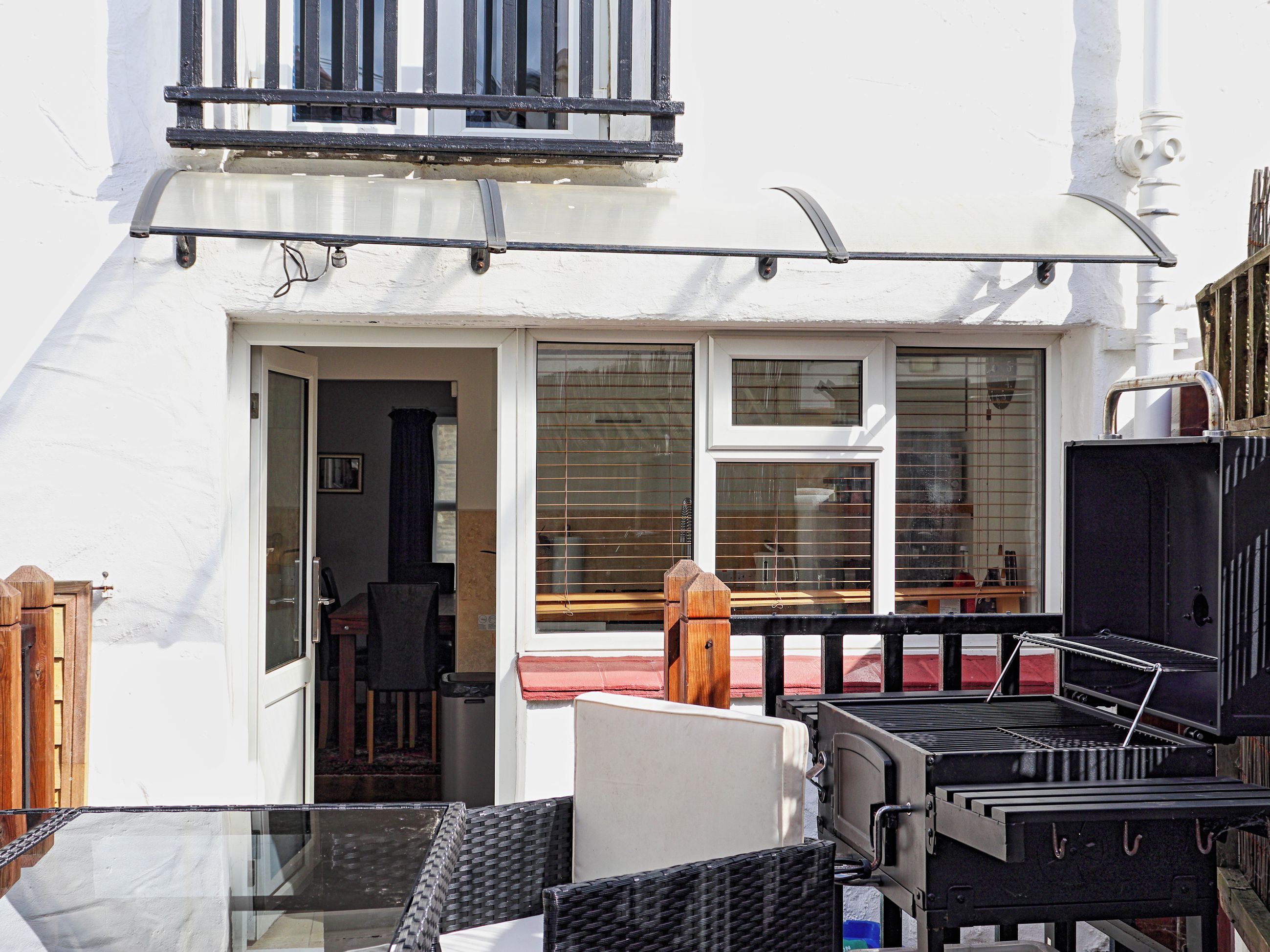 Un balcón con una parrilla, un comedor con sillas y una ventana con persianas.