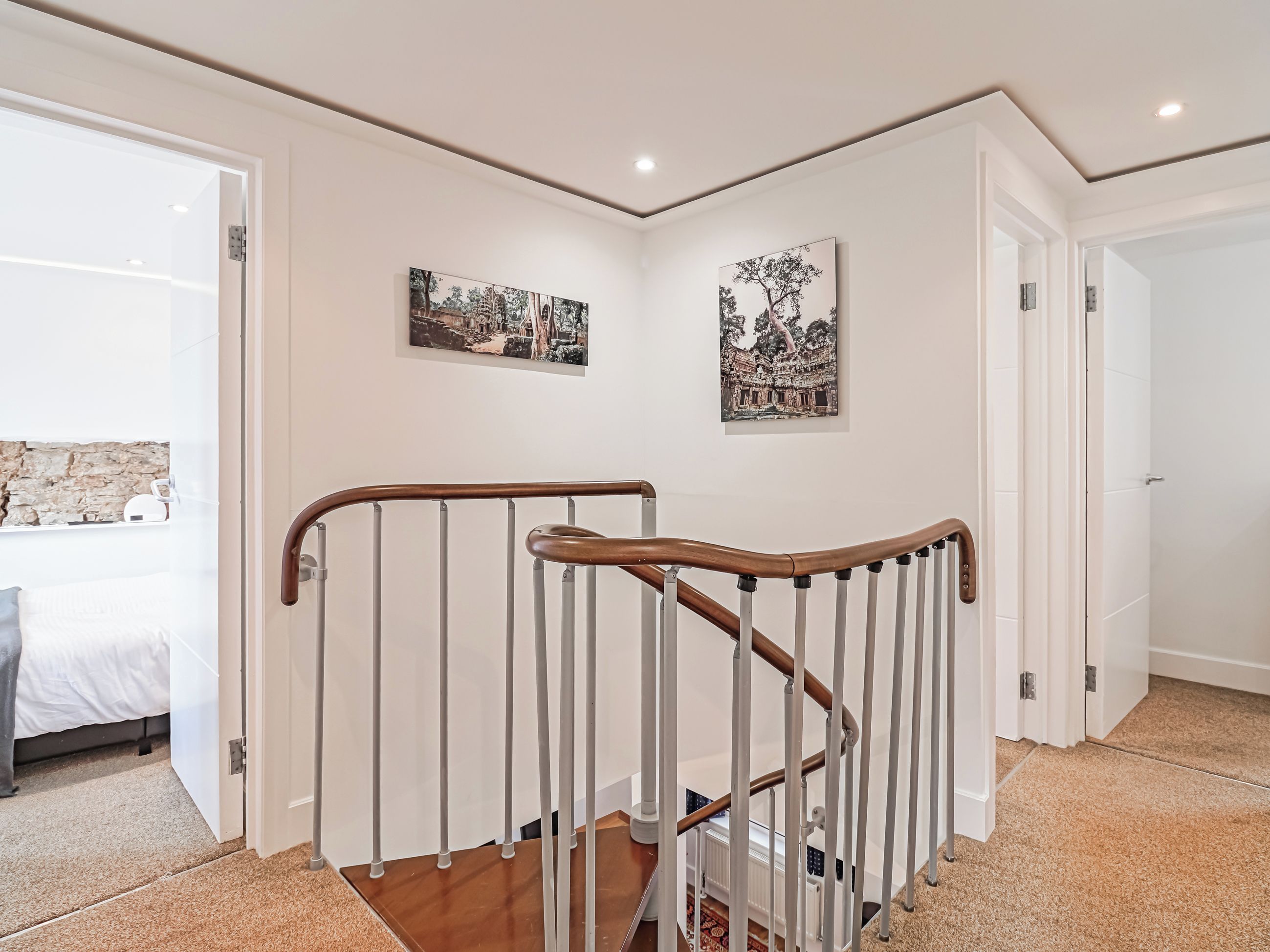 Una escalera con barandilla de madera y balaustres blancos, que conduce a un dormitorio con cama y pared de piedra.