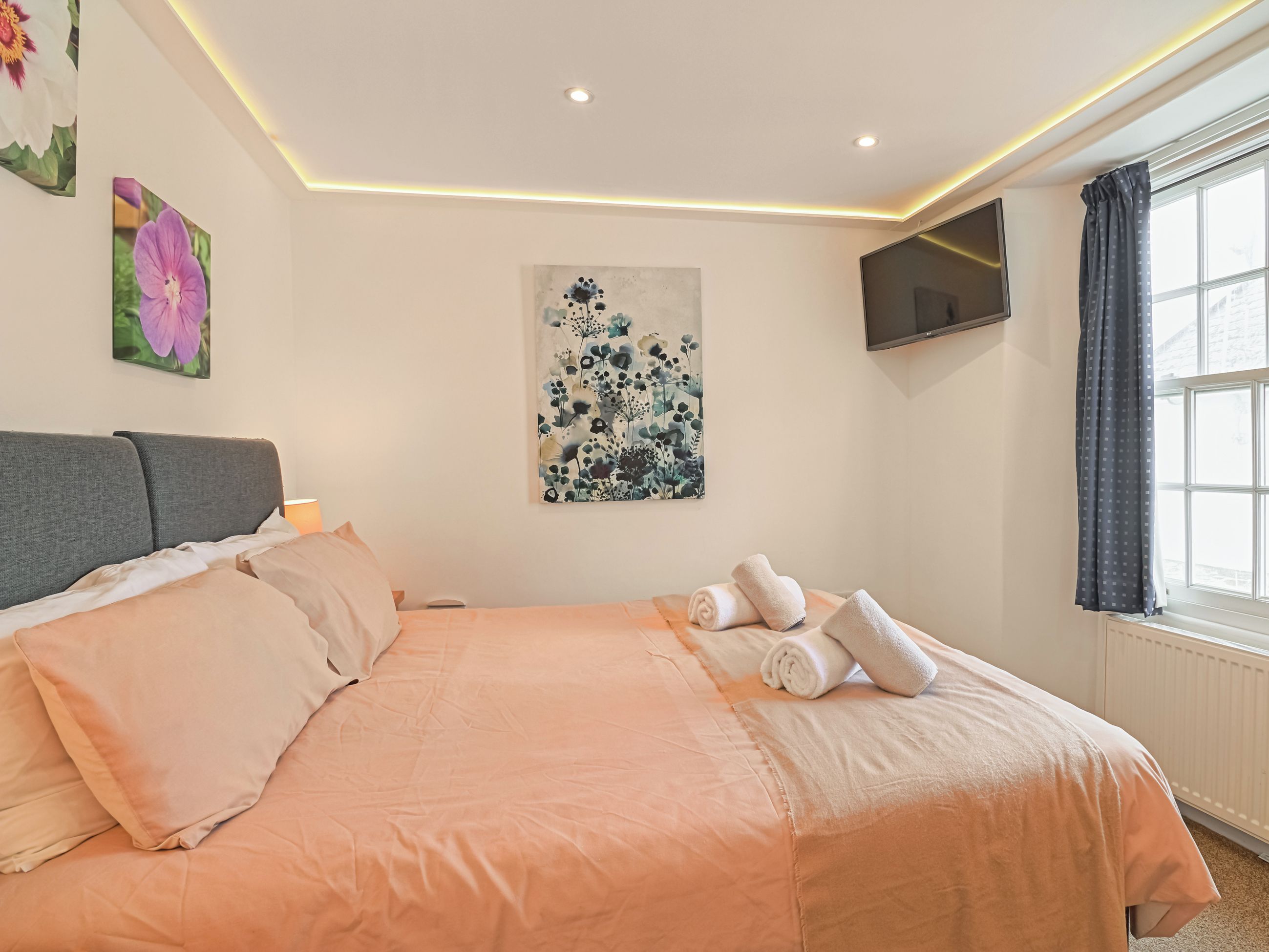 Habitación de hotel con cama, almohadas, televisión de pantalla plana, obras de arte y ventana con cortinas.