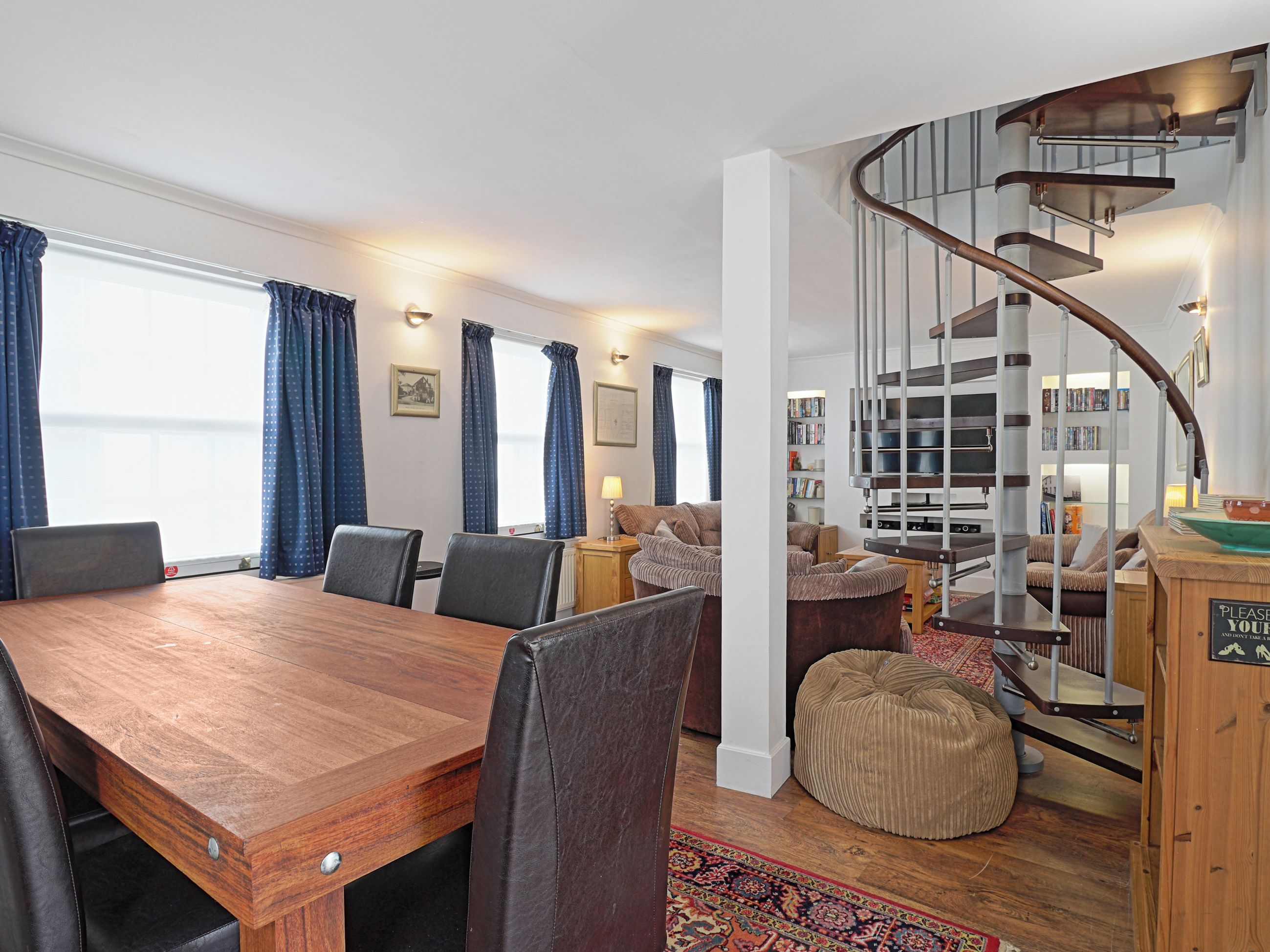 Un interior moderno con una mesa de comedor de madera, sillas, una escalera en espiral y una zona de estar acogedora.