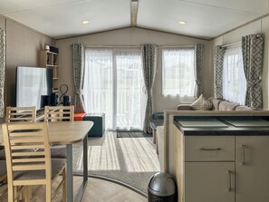 Een knus woongedeelte met een eettafel, stoelen, een bank, een televisie en een kitchenette.