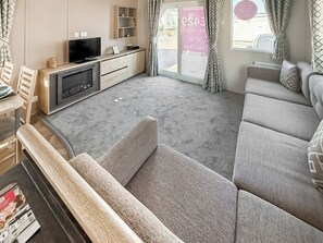 A modern living room with a sofa, a flat-screen TV, a fireplace, and a window with curtains. - Northfield Lodge 2 - UK52396 (Skipsea Sands)