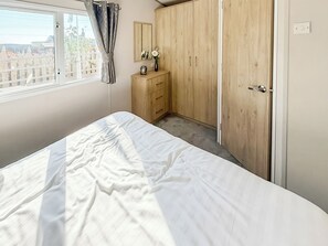 A bedroom with a bed, a wardrobe, a dresser, a mirror, and a window with curtains. - Northfield Lodge 2 - UK52396 (Skipsea Sands)