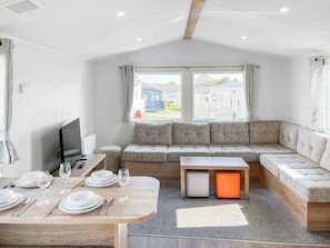 Ein modernes Wohnzimmer mit einer Couch, einem Fernseher und einem Esstisch für vier Personen.