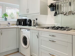 A modern kitchen with a built-in washing machine, a gas stove, and various kitchen utensils hanging on the wall. - 2 bedroom accommodation in Teignmouth (Teignmouth)