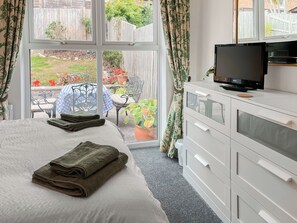 A bedroom with a bed, a television on a dresser, and a view of a garden through a window. - 2 bedroom accommodation in Teignmouth (Teignmouth)