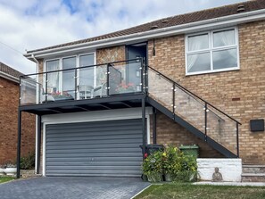 A residential building with a garage, a balcony with glass railings, and a brick facade. - 2 bedroom accommodation in Teignmouth (Teignmouth)