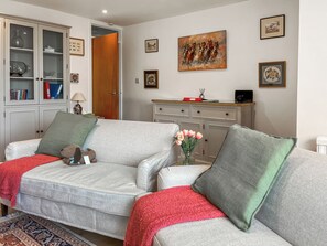 A living room with a grey sofa, a red throw blanket, a teddy bear, a vase of tulips, and a cabinet with glass doors. - 2 bedroom accommodation in Teignmouth (Teignmouth)