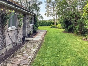 A stone pathway leading to a house with a well-maintained lawn and surrounding greenery. - 3 bedroom accommodation in Dornoch (Dornoch)