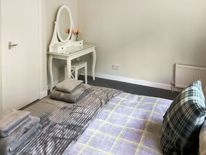 A bedroom with a bed, a bedside table, a mirror, and a radiator. - 3 bedroom accommodation in Dornoch (Dornoch)