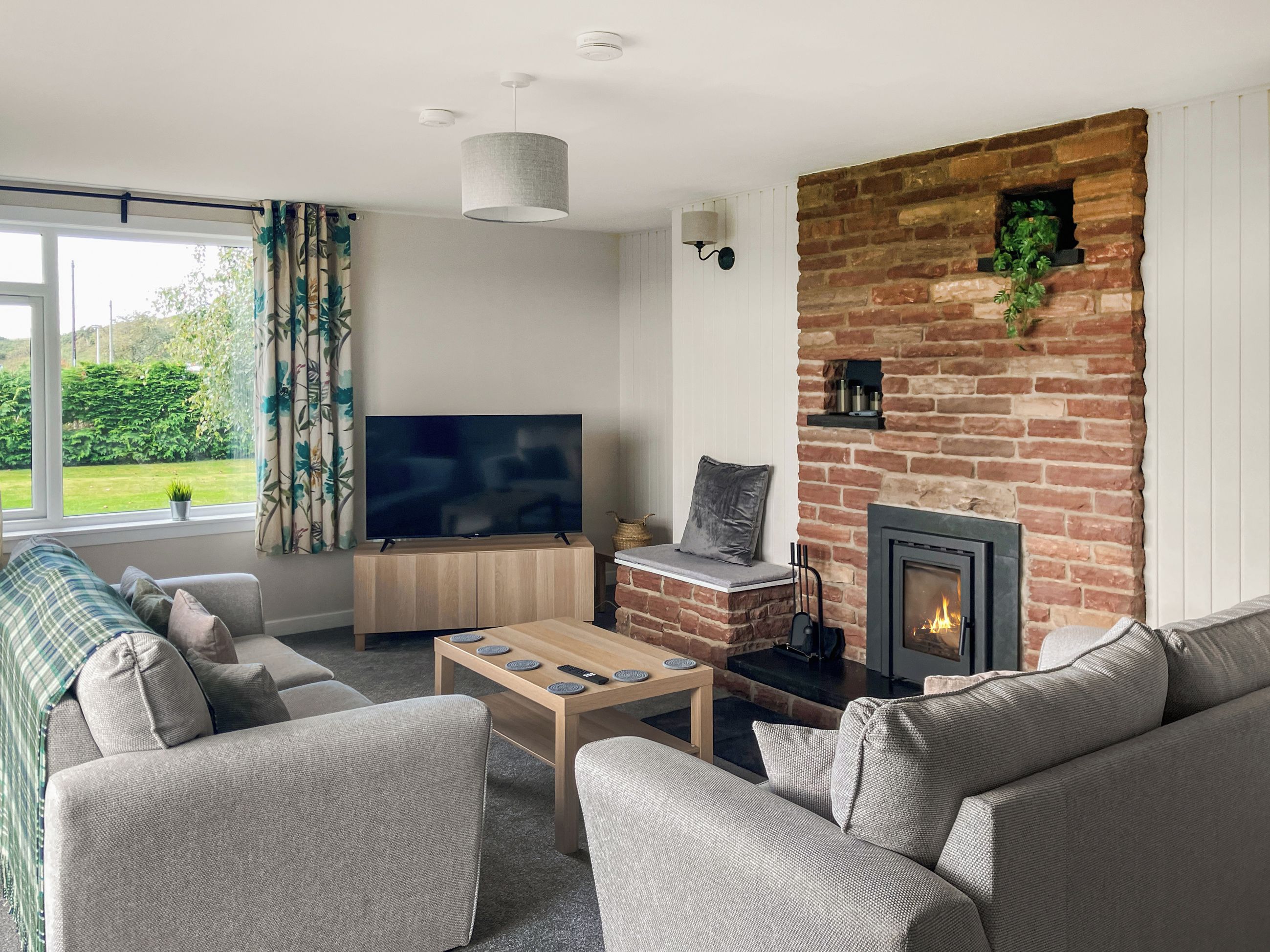 A living room with a television, sofa, coffee table, fireplace, and a view of greenery outside.
