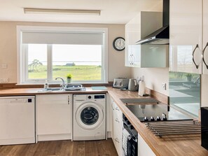 A compact kitchen with a built-in washer and dryer, a window with a view, and a clock on the wall. - 3 bedroom accommodation in Dornoch (Dornoch)