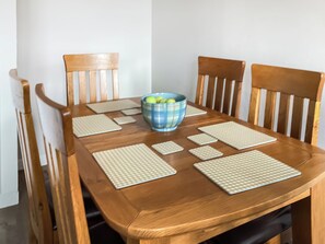Une table de salle à manger en bois, accompagnée de quatre chaises, d’un saladier bleu contenant des pommes et de quatre sets de table.