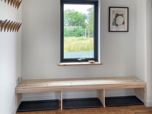 Ein Zimmer mit einer hölzernen Sitzbank, einem Fenster mit Blick ins Grüne und einem gerahmten Bild an der Wand.