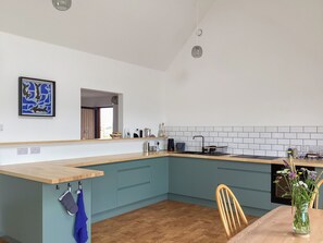 Eine moderne Küche mit einer Holz Arbeitsplatte, blauen Schränken und einem Essbereich mit Holztisch und Stühlen.